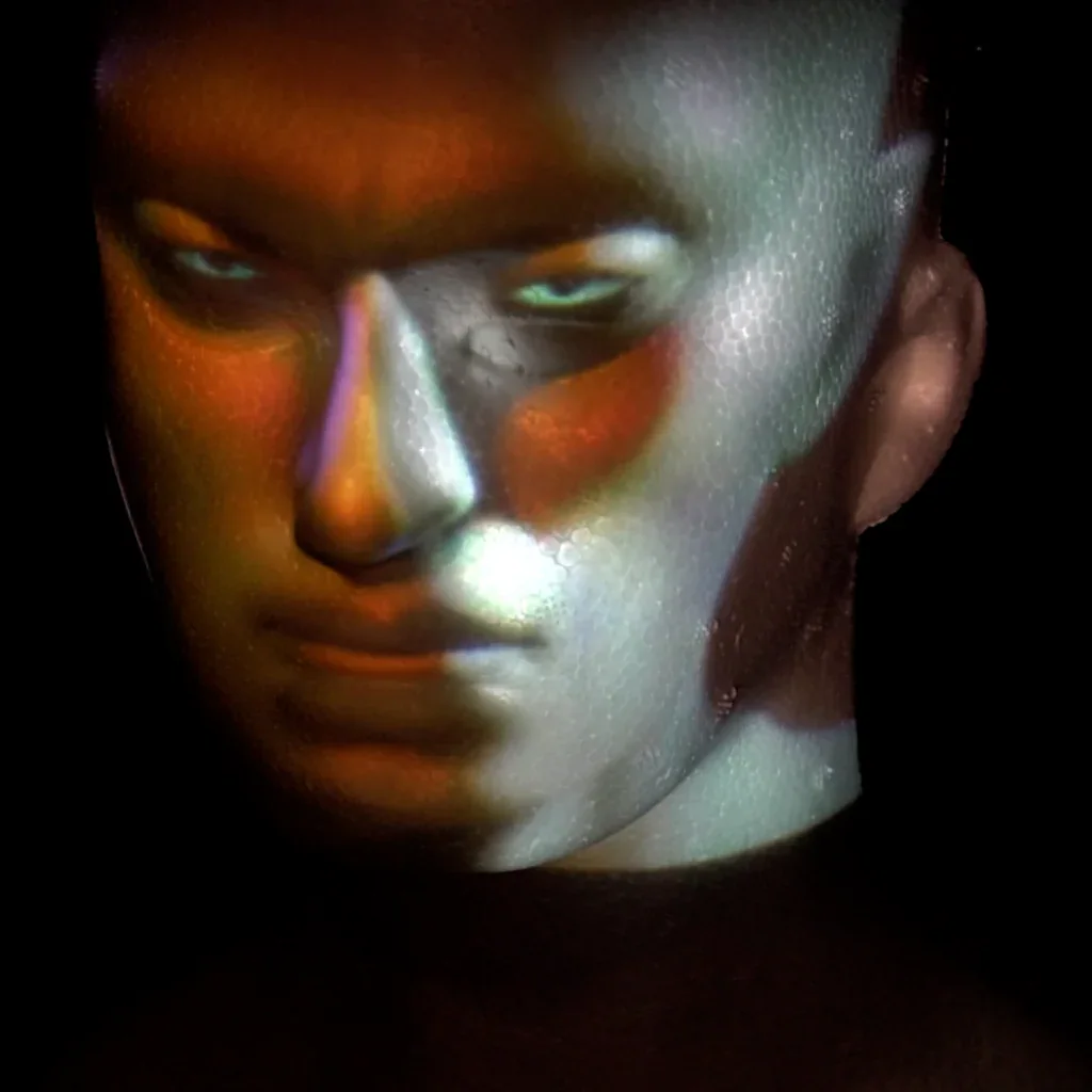 AI projection · Studio R&D Coloured AI-generated facial imagery projected onto a sculpted head against a dark background.